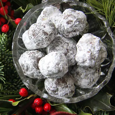 A bowl of powdered sugar covered cookies on top of christmas decorations.