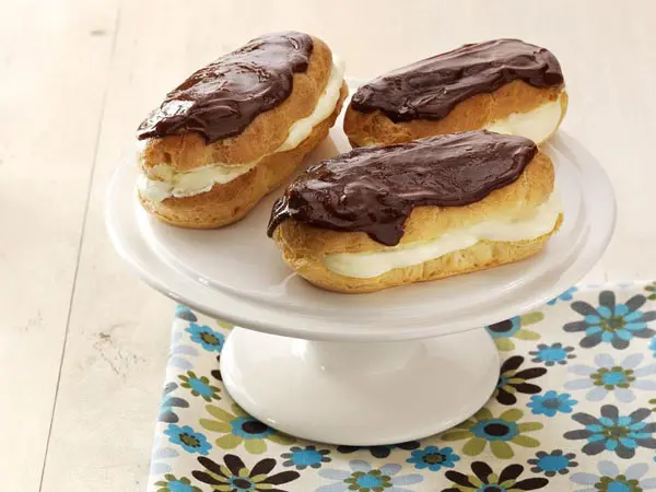 Three chocolate covered eclairs on a white cake plate.