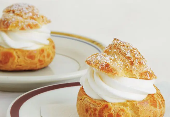 Two pastries on plates with whipped cream and sugar.