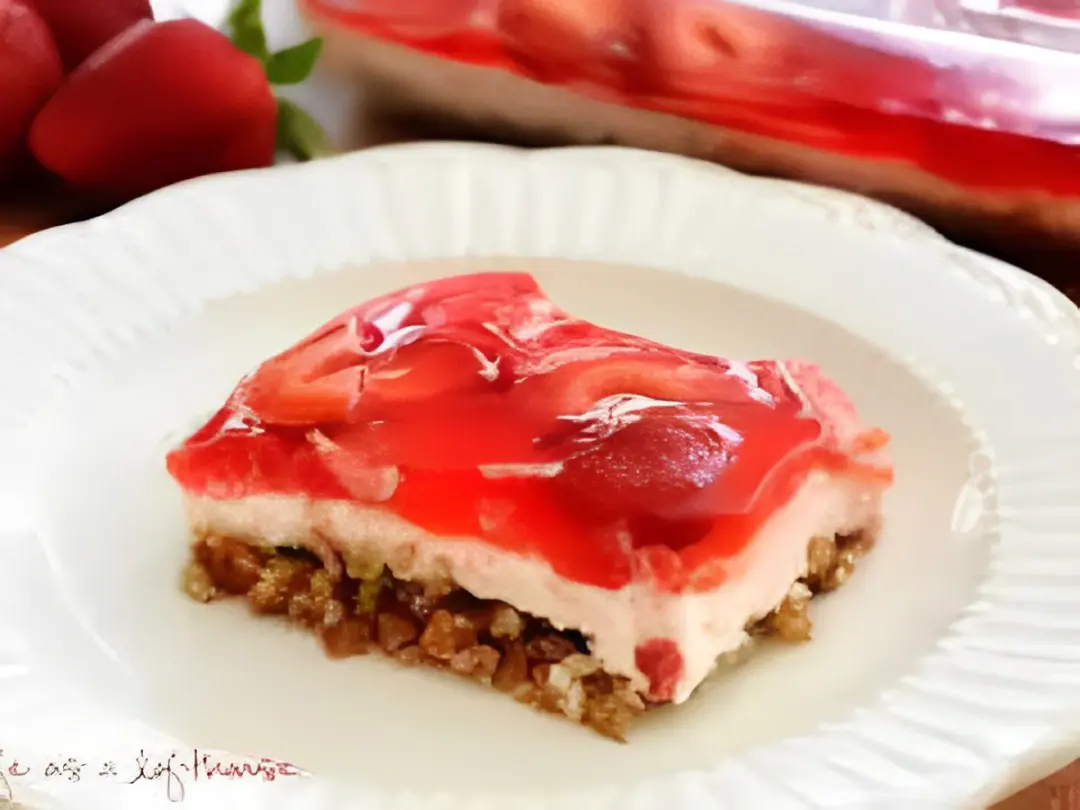 A piece of strawberry cheesecake dessert on top of a paper plate.