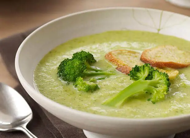 A bowl of broccoli soup with bread on the side.