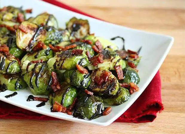 A white plate topped with cooked brussel sprouts covered in sauce.