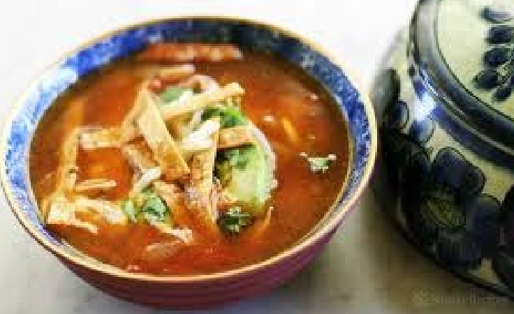 A bowl of soup with tortilla strips and avocado.