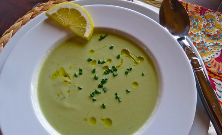 A bowl of soup with lemon and chives on top.