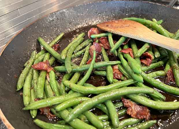 A pan of green beans with bacon in it.